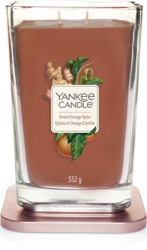 Duży brązowy świeca zapachowa w przezroczystym szklanym pojemniku z etykietą Yankee Candle. Ilustracje przedstawiają pomarańczę i przyprawy.