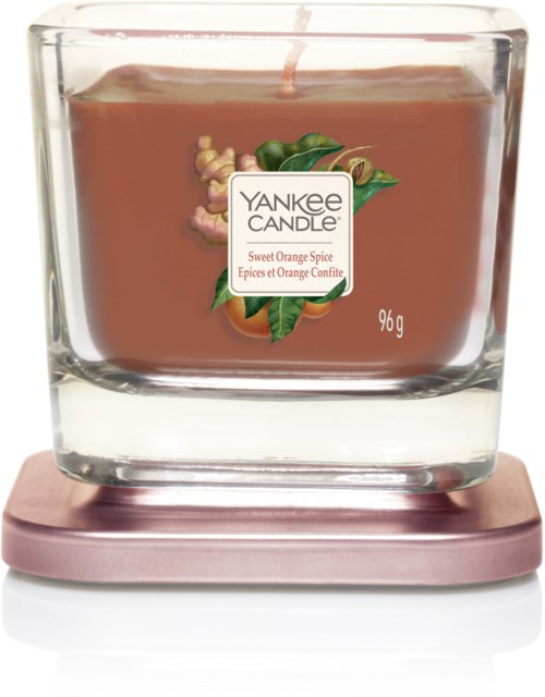 Świeca zapachowa w szklanym pojemniku, marka Yankee Candle, o zapachu pomarańczy i przypraw, na różowej podstawie.