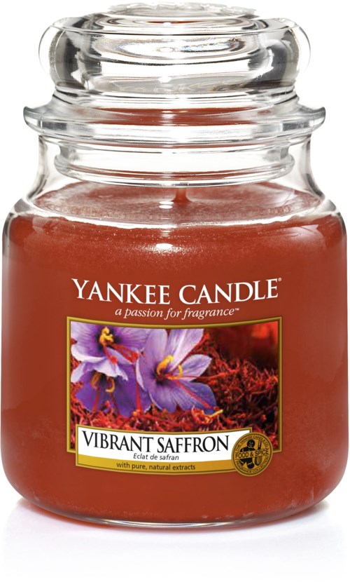 Et rødt lys i en glasbeholder, mærket 'Vibrant Saffron' med lilla blomster på forsiden.