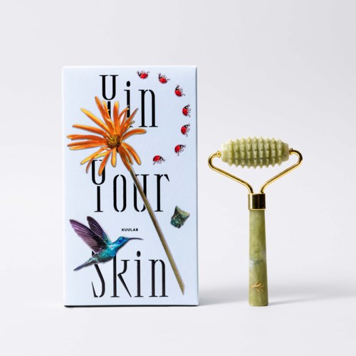 A skincare product with a box displaying a flower, a bird, and ladybugs, along with a jade roller.