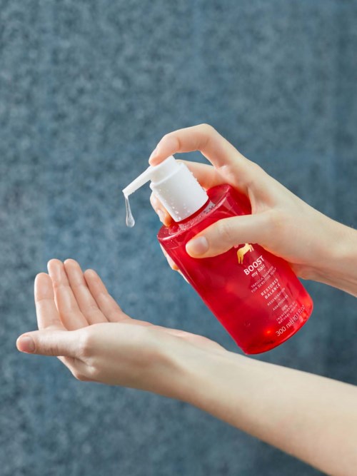 A person dispensing liquid from a red bottle with a pump onto their hand.