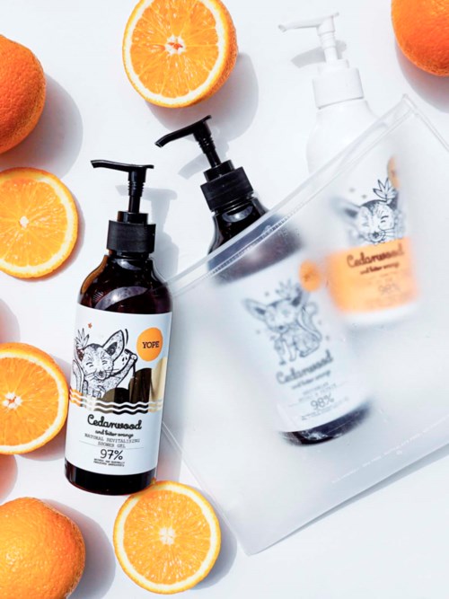 Två apelsinhalvor och hela apelsiner omger två pumpflaskor med lotion eller tvål med tigerlogo och en genomskinlig väska.