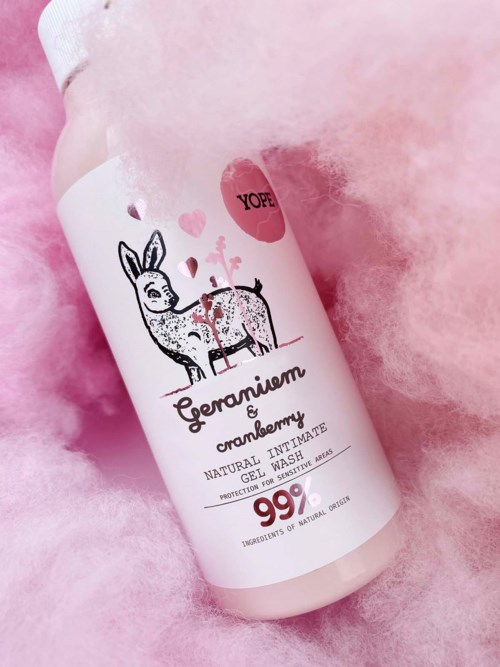 En vit flaska ligger på rosa fluffigt tyg med sött renhjärta och hjärtan, märkt 'Geranium Cranberry' för intimgelvask.