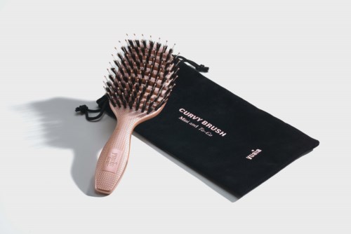 En trähårborste med svarta piggar och en svart påse märkt "Curly Brush" ligger på en vit yta.