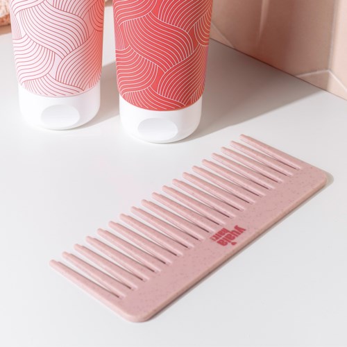 To flasker og en rosa kam ligger på en hvid overflade, med flaskerne med matchende pink design og en pink logo.