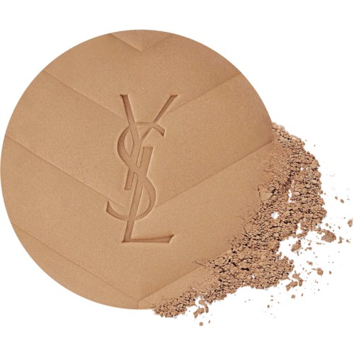 A round makeup powder compact with Yves Saint Laurent logo, some powder spilled beside it.