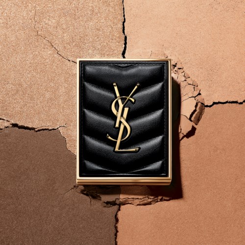 En sort læderæske med et guld YSL-logo, placeret på en sprukken beige væg.