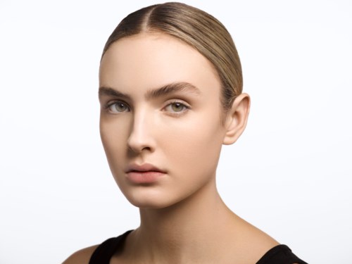 A young woman with smooth skin, neutral expression, and light brown hair tied back, wearing a black top.