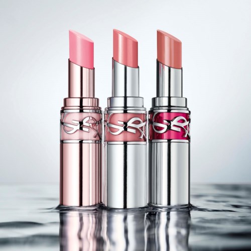 Tre leppestifter i rosa, nude og ferskenfarger står oppreist på en reflekterende overflate.