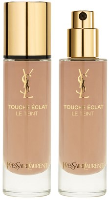 Två flaskor av Yves Saint Laurent Touche Éclat Le Teint foundation, guldkapslar, beige flytande innuti.