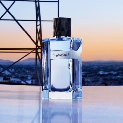 En Yves Saint Laurent-parfymeflaske foran en bysilhuett ved solnedgang.