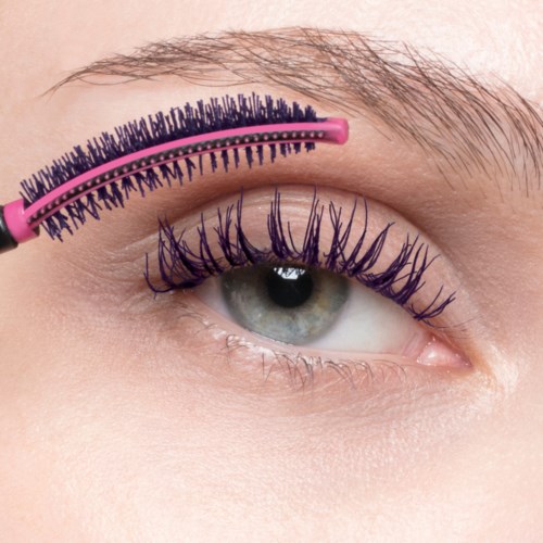 Een close-up van een persoon met een groen oog, die paarse mascara gebruikt om de wimpers te accentueren.