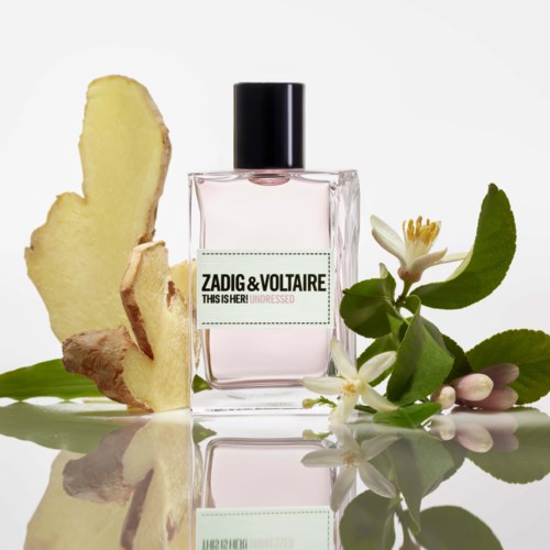 En parfymflaska märkt Zadig & Voltaire omgiven av ingefärsskivor, vita blommor och gröna blad.