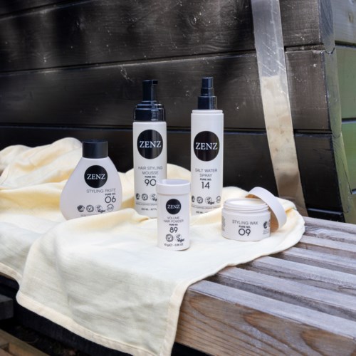 Hårstylingprodukter inklusive spray, mousse, saltvattenspray, stylingpasta och vax visas på en träyta.
