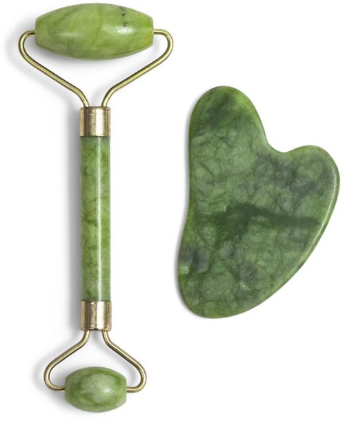 En grön jade ansiktsrulle och ett jade gua sha-verktyg används för hudmassage och förbättrad hudhälsa.