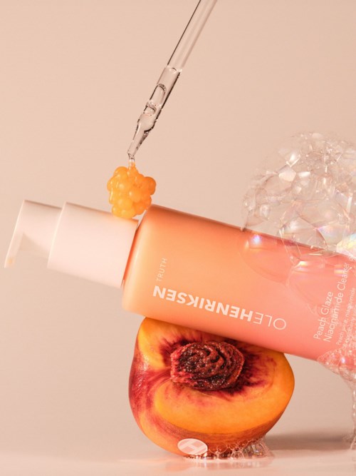 En fersken med et hudpleieprodukt og isbiter på toppen, med et pipette over. Myk rosa bakgrunn.