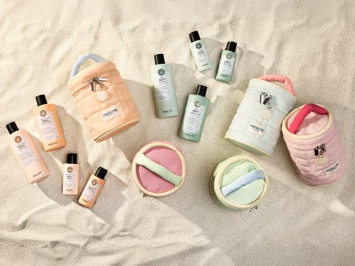 Strandrelaterad hudvårdsprodukter och tillbehör placerade på sand, inklusive lotioner, krämer och påsar i pastellfärger.