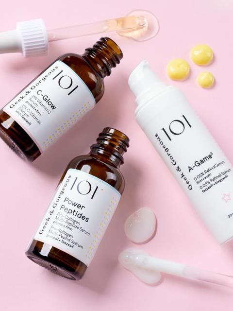 Skincare bottles and creams on a pink background with droppers and tablets.