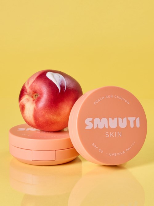 En fersken ligger på en rosa beholder merket Smuuti Skin, med en annen beholder ved siden av, mot en gul bakgrunn.