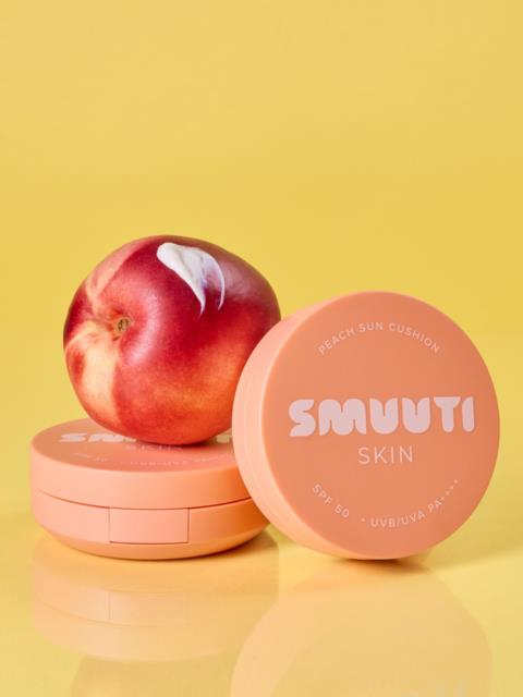 En fersken ligger på en rosa beholder merket Smuuti Skin, med en annen beholder ved siden av, mot en gul bakgrunn.