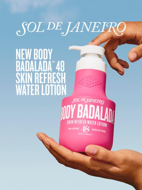 Eine Hand hält eine pinke Flasche von Sol de Janeiro Badalada Körperlotion und Wasser gegen blauen Himmel.