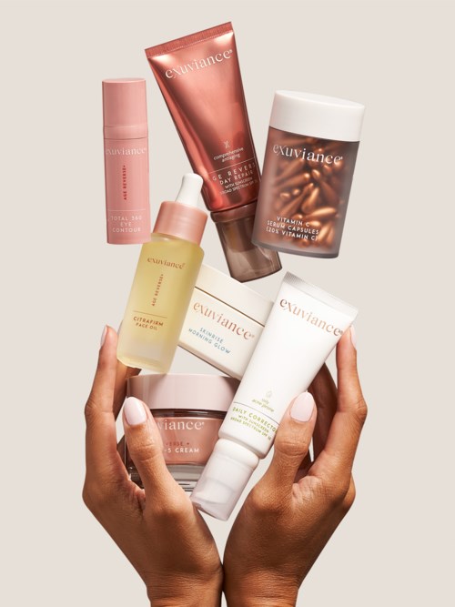 Hænder holder forskellige hudplejeprodukter, herunder cremer og serum, i forskellige flasker og tubes, pænt arrangeret.