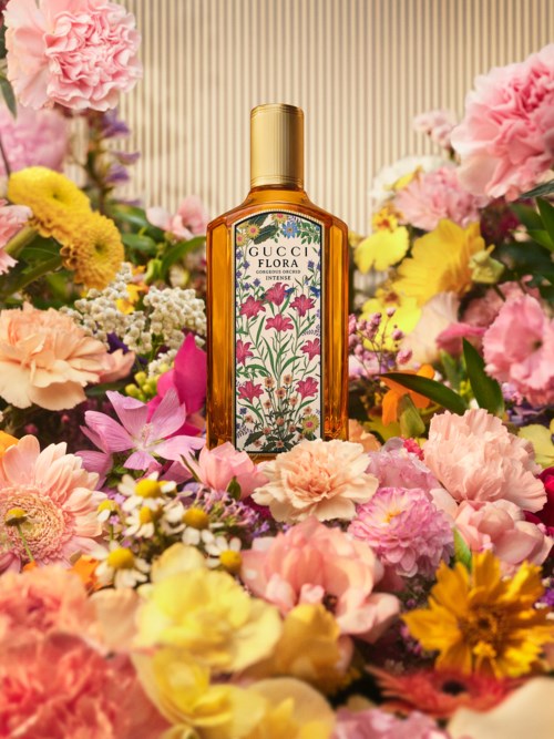 Gucci Flora-parfymflaska omgiven av färgglada blommor i en livfull presentation.