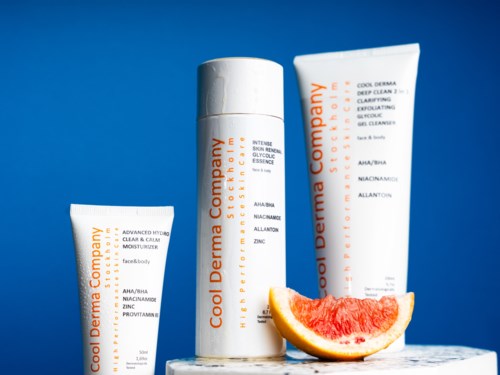 Cool Derma Company hudvårdsprodukter med en skiva grapefrukt, placerade på en yta mot en blå bakgrund.