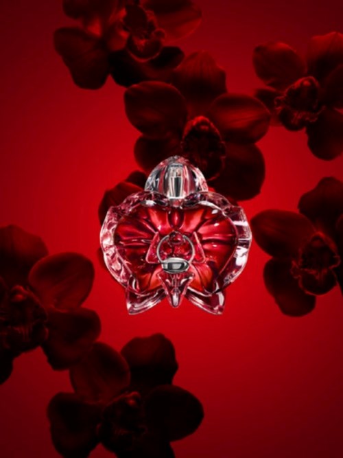 En floral parfyllflaska med facetslipad glasdesign, omgiven av mörkröda blomblad på en röd bakgrund.