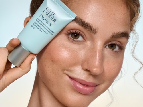 En kvinna med klar hy håller en blå tub med Estée Lauder DayWear ansiktskräm nära sitt ansikte.