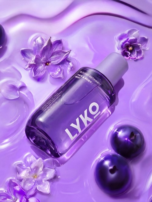 Lyko-merkkinen pullo violetteja kukkia ja kiiltäviä violetteja palloja ympärillä violetilla taustalla.