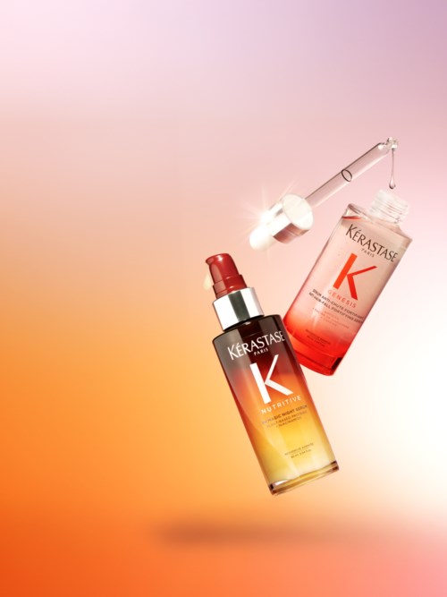 A Kerastase hair essence bottle with a dropper and a box are displayed against a soft orange-pink background.