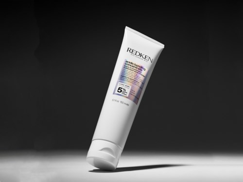 Redken hair product tube with a white body, purple and black label, on a dark background.