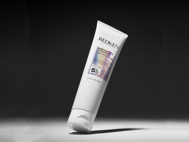 Redken hair product tube with a white body, purple and black label, on a dark background.