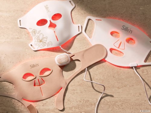 Drie gezichtsvermaskingen met LED-lichten voor huidverzorging, sommige met bloemenontwerp, op een beige oppervlak.