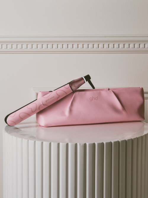 En rosa locktång med ett rosa skydd i en matchande rosa väska på ett vitt runt bord.