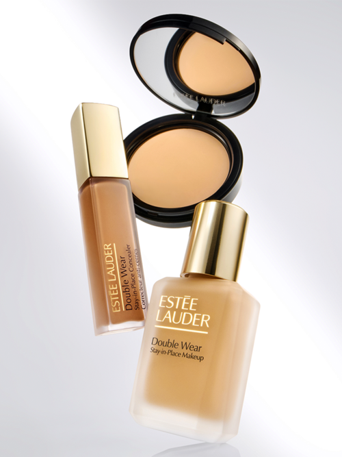 Två Estée Lauder Double Wear makeupflaskor, en kompakt med spegel, alla med guldlock och beige toner.