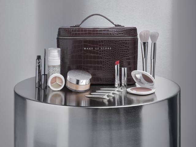 Makeup- och hudvårdsprodukter, borstar, verktyg och en brun makeupväska på ett runt bord.