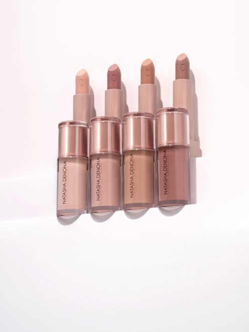 Vier lippenstiften in neutrale tinten met doorzichtige doppen en etiketten, rechtop op een witte achtergrond.