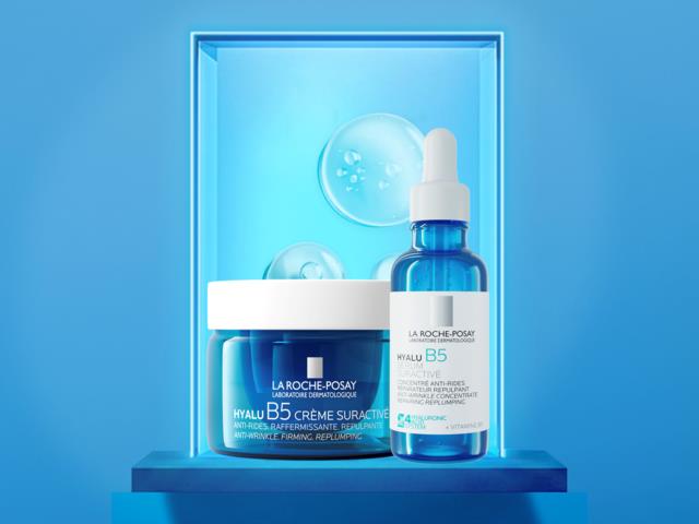 La Roche-Posay hudvårdsprodukter Hyalu B5 kräm och serum visas på en blå hylla med en glödande blå bakgrund.