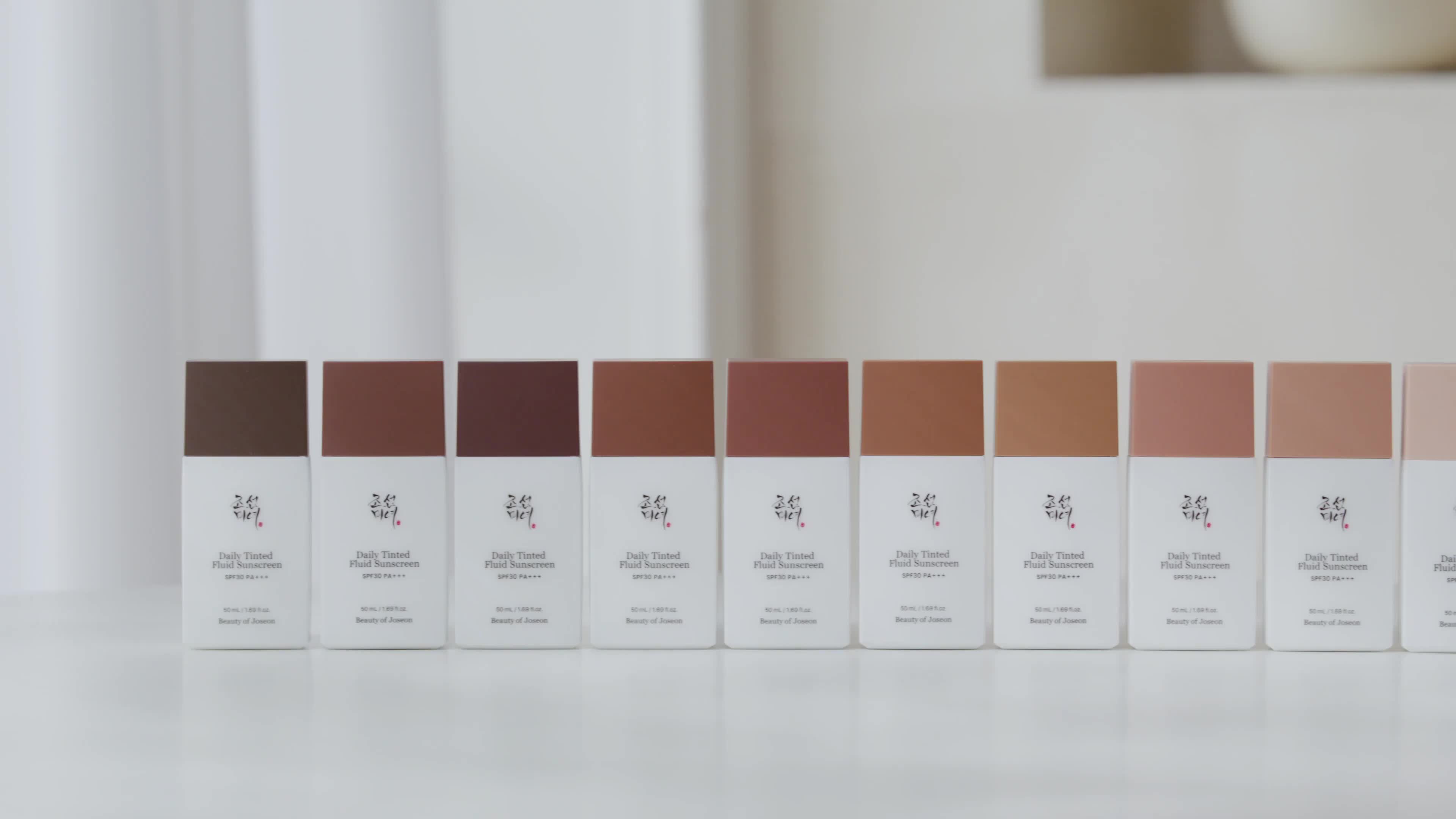 Several boxes of skincare or beauty products are arranged in a line on a white shelf. Each box has a different shade of brown.