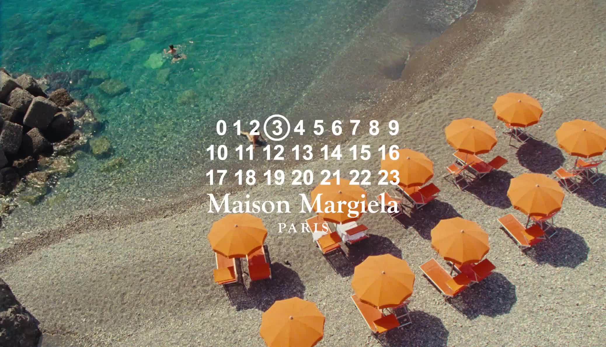 Beach with orange umbrellas, chairs, clear water, and people swimming. Maison Margiela branding overlayed on the scene.
