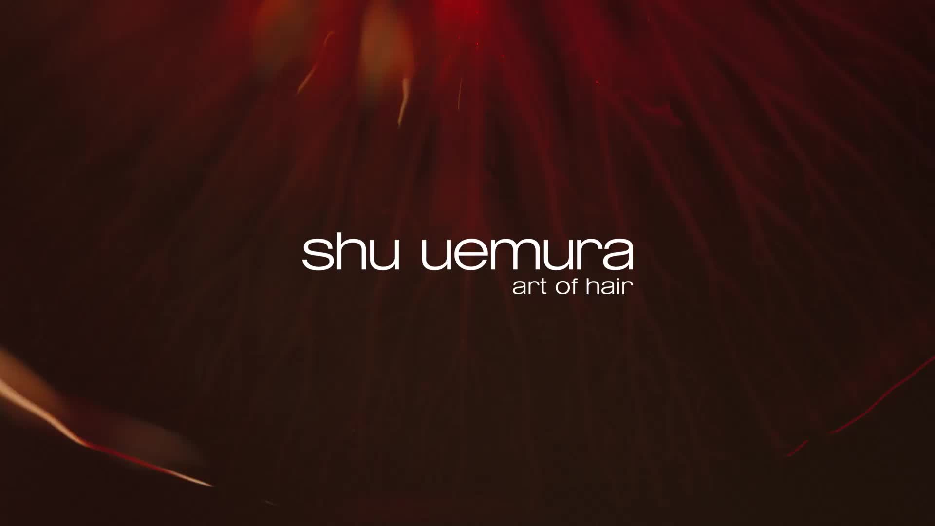 Logo Shu Uemura z napisem "art of hair" pod, na ciemnym, płomiennym tle.