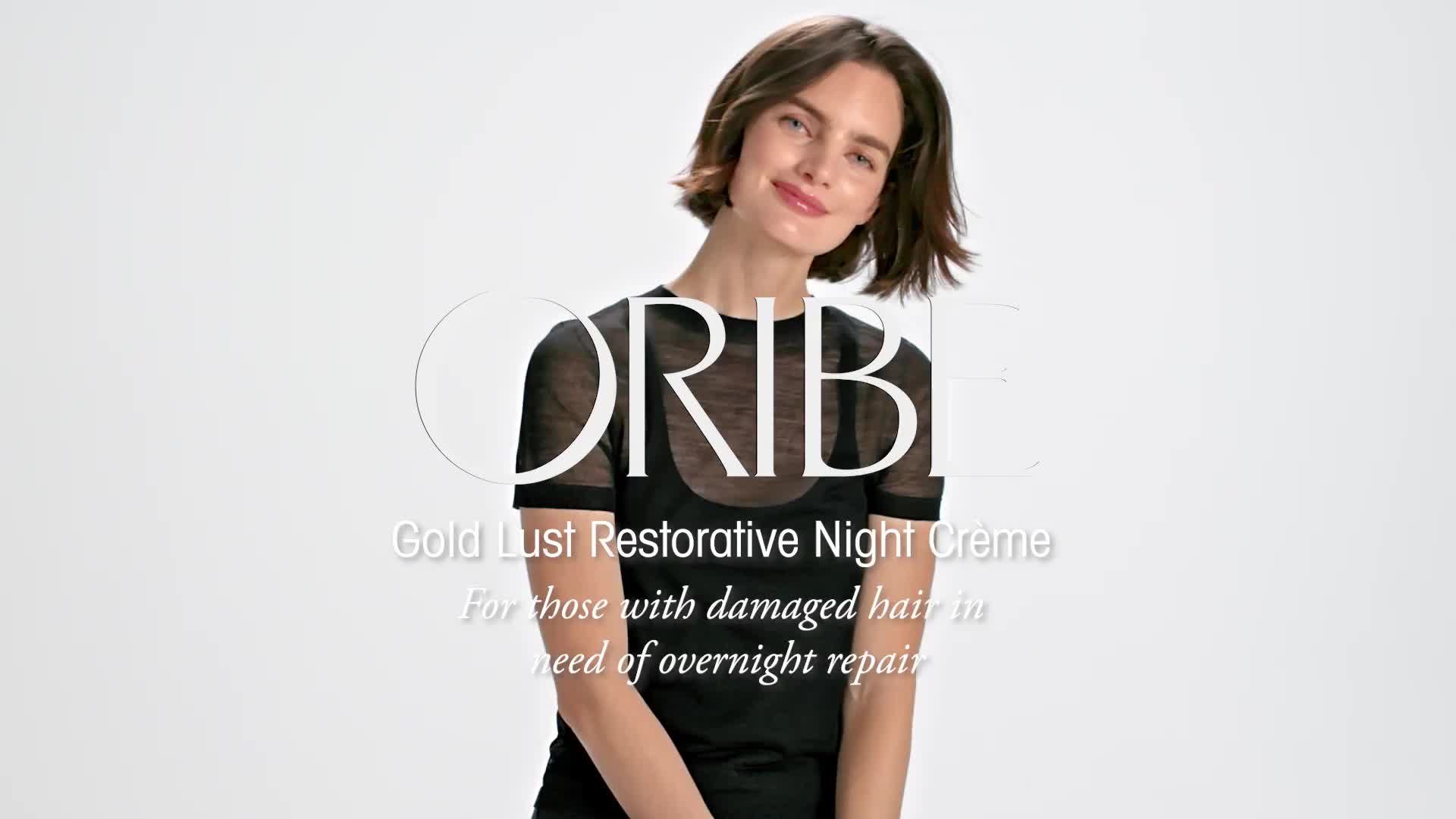 Eine lächelnde Frau mit kurzen braunen Haaren in schwarzem Top, die ORIBE Gold Lust Restorative Night Creme bewirbt.